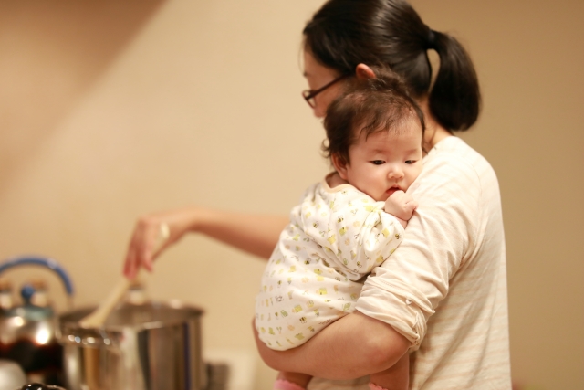 赤ちゃんを抱っこしながら料理する女性